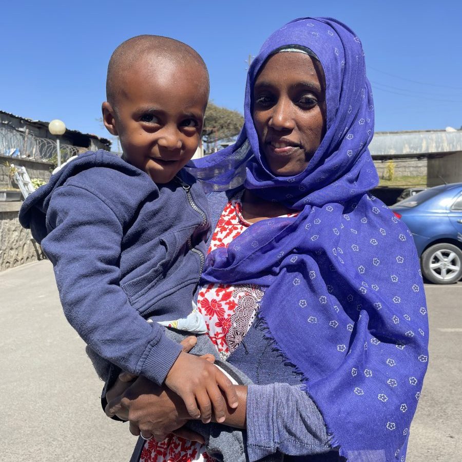 A mother in a purple headscarf, holding her little boy, both smiling