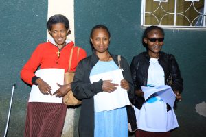 3 women smiling and holding their Braille information leaflets.